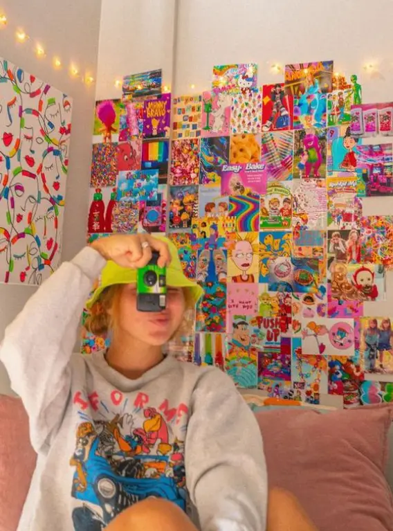 Mulher tirando foo do look moletom com bucket hat no quarto com painel kidcore