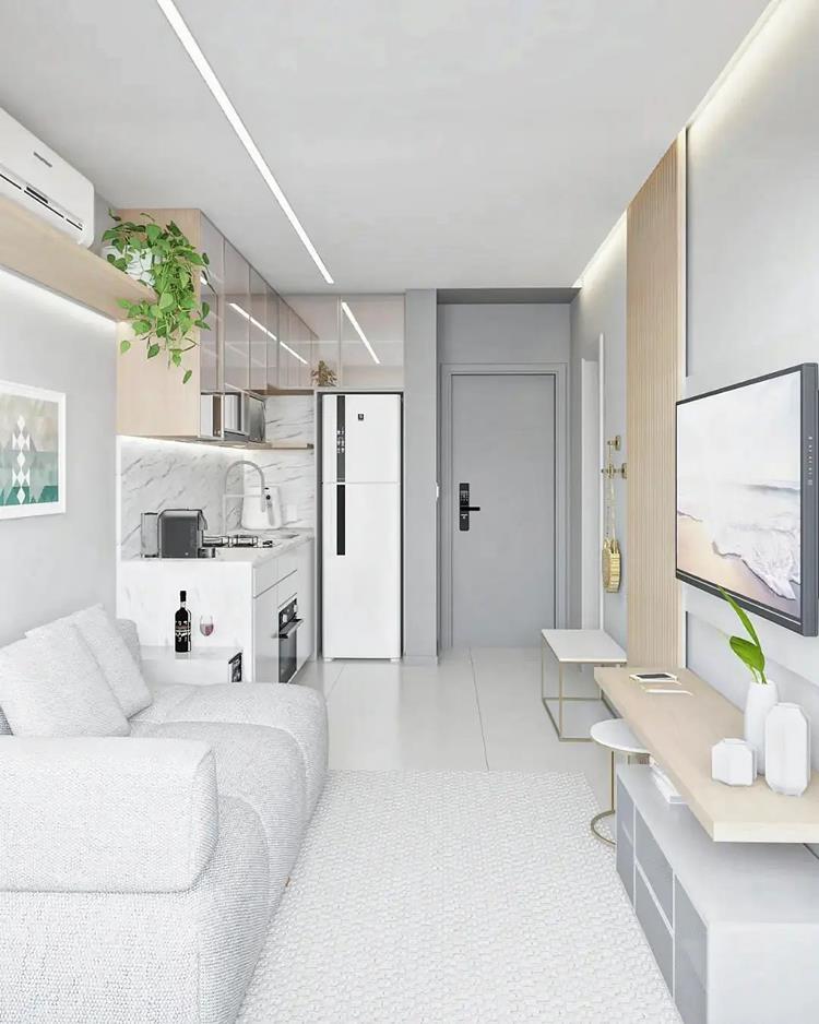 foto de sala e cozinha em apartamento pequeno, tons de branco e cinza claro, som sofá cinza, TV na parede, geladeira branca e mais 