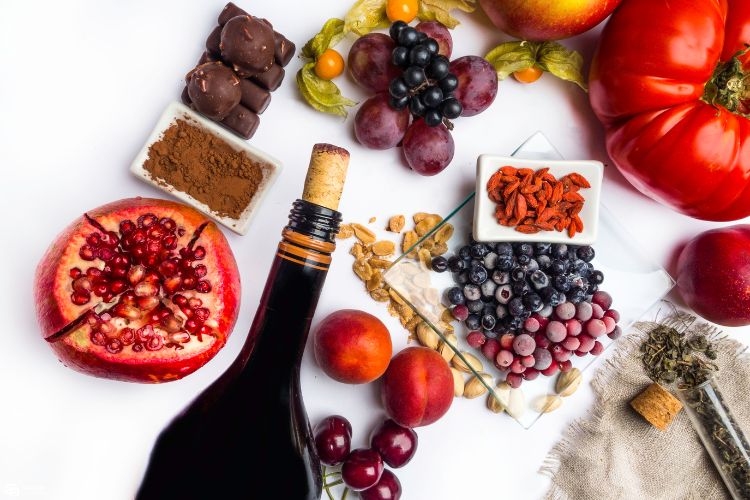 Foto de futas como uva, mirtilo, romã, além de garrafa de vinho tinto e cacau