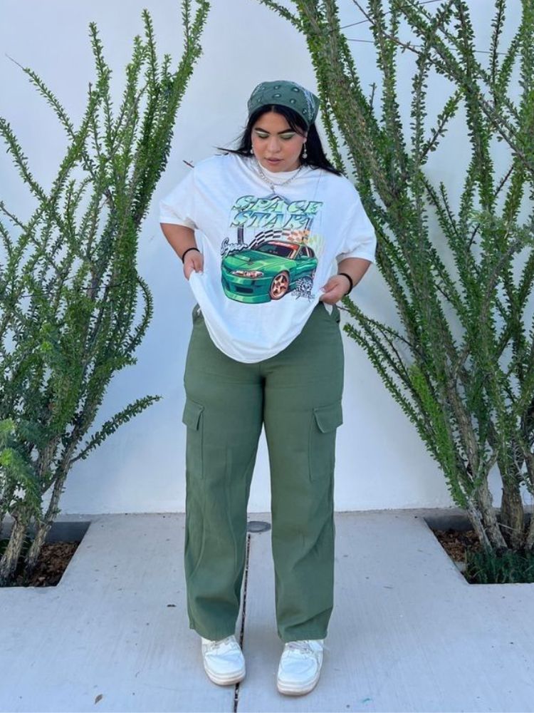 Mulher de pele clara usando look com camiseta oversized, calça cargo verde e bandana amarrada na cabeça. 