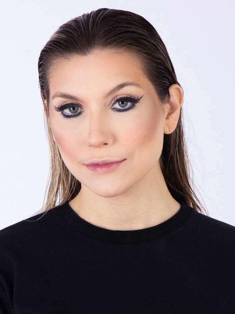 Mulher de pele clara com rosto higienizado e cabelo umedecido, usando blusa preta, base clara, contorno e delineado