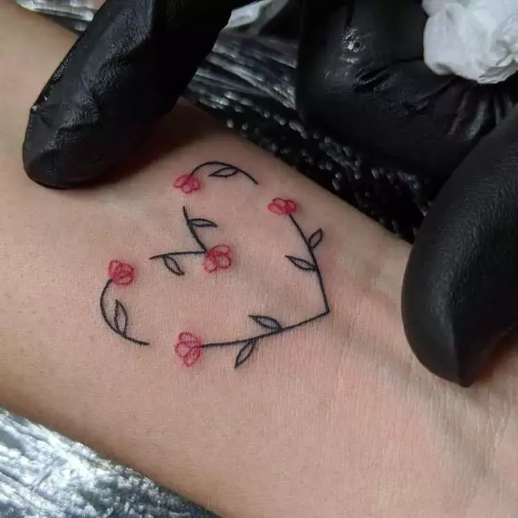 tatuagem na parte inferior do braço, contorno de coração com folhas e flores vermelhas