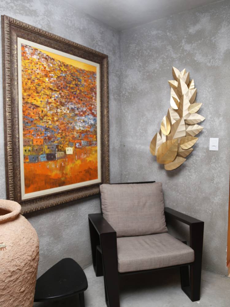 Esapço com poltrona cinza, vaso bege e quadro laranja, além de parede em cinza feita com restos de argamassa de assentamento de piso, de cimento e de gesso, com uma folha dourada de enfeite