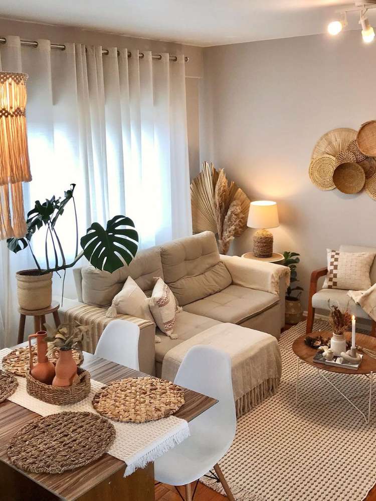 Costela-de-adão no canto de uma sala em bege, com sofás e poltronas claras, mesa bege com decorações em bege e outros itens decorativos nessa paleta de cores
