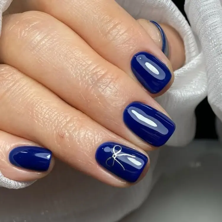 Foto de mão com unhas curtas quadradas em azul marinho com laço no anelar 