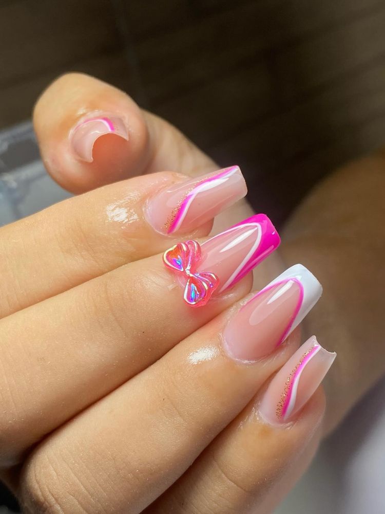 Pessoa de pele clara com unha nude decorada em rosa e com laço rosa no dedo do meio