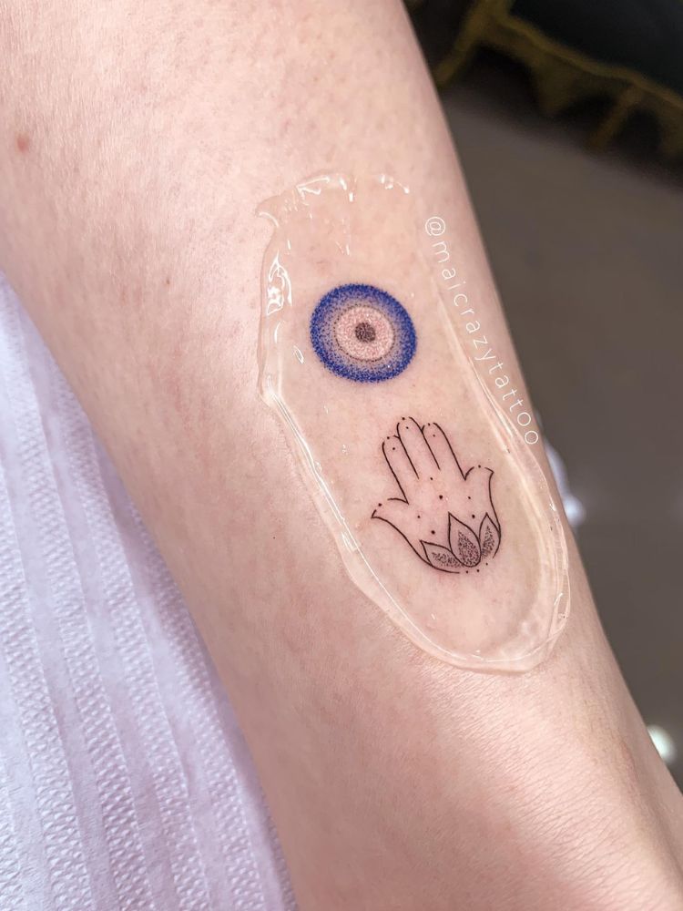 Tatuagem de olho-grego em azul e branco, além de mão de fátima em fineline