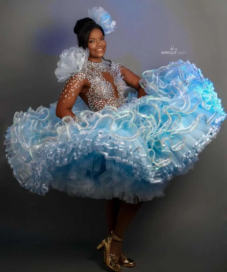 Imagem de uma rainha da quadrilha em festa junina, vestindo um deslumbrante vestido azul claro com saia volumosa e corpete bordado com pedrarias. Ela sorri para a câmera, exibindo um penteado elegante, capturando a energia festiva e a beleza da celebração.