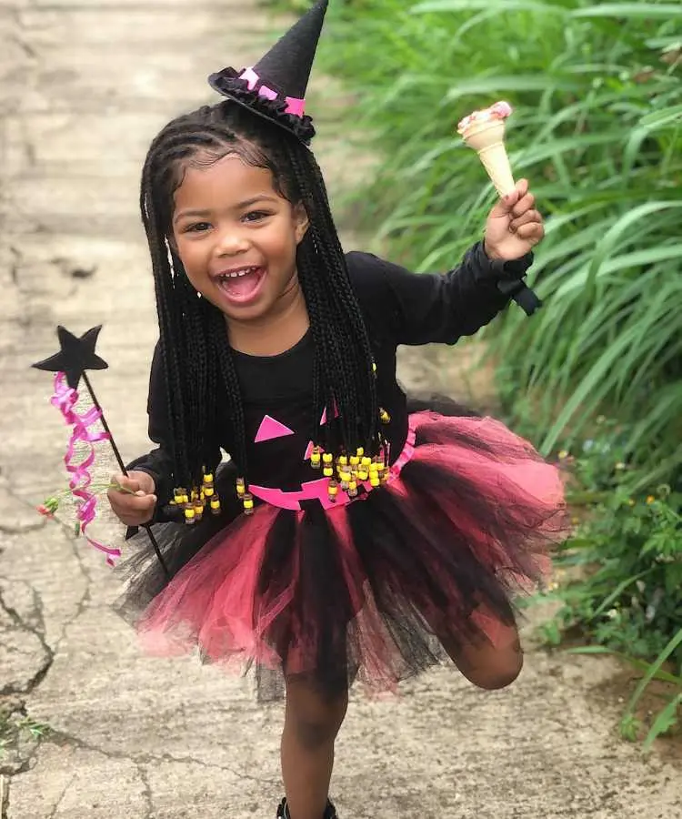 Garota fantasiada para o Halloween: Cores predominantes: preto e pink. Usa: body manga cumprida personalizado com carinha de abóbora, saia de tule, tiara de mini-chapéu pontudo, segura varinha e sorvete