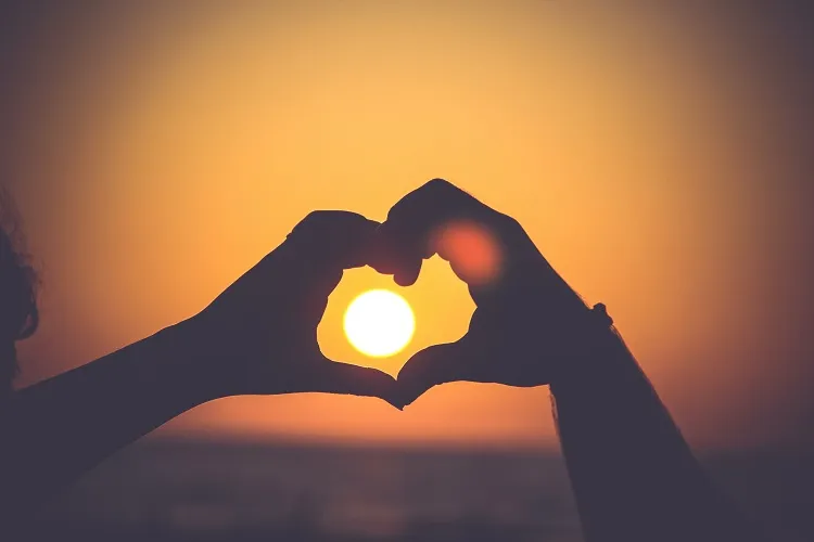 casal fazendo coração com as mãos no pôr do sol