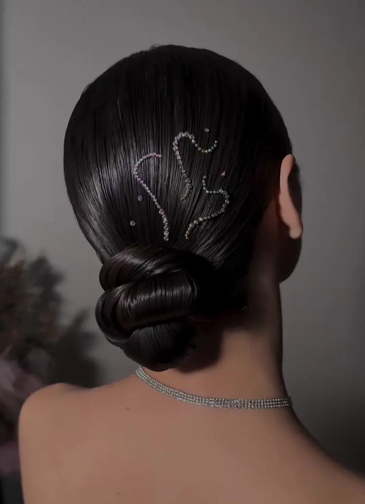 Mulher de pele clara de costas com cabelo castanho em coque baixo com strass