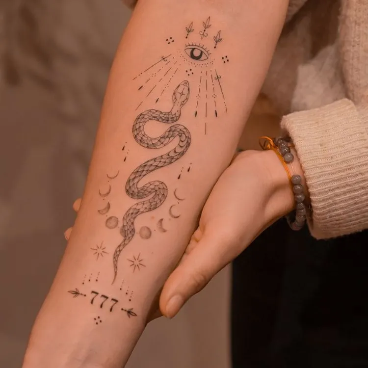 tatuagem de cobra com as fases da lua ao redor, um olho no topo e os números 777 em baixo