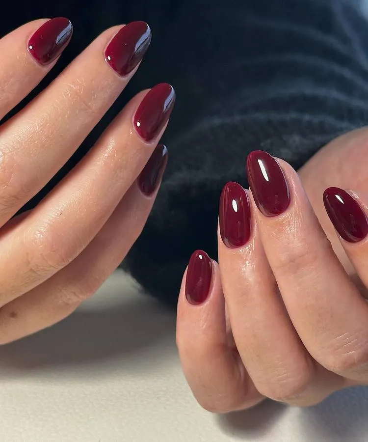 Mãos femininas com unhas amendoadas médias e elegantes na cor vermelho cereja.
