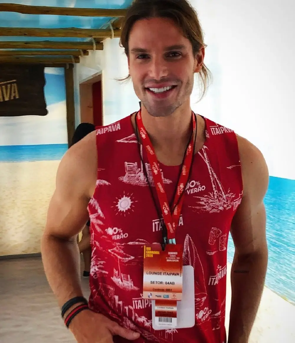 Jonatas Faro sorrindo em pé, com crachás no pescoço e com a camiseta da marca de cerveja Itaipava
