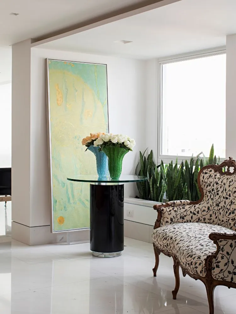 Foto de hall de entrada branco com quadro colorido ao fundo, mesa com vasos de flores, poltrona clara com desenhos pretos e flores ao fundo 