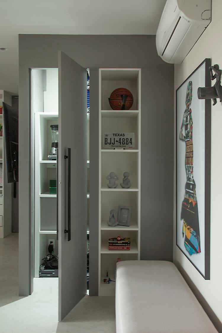 foto de porta branca com puxador preto aberta, prateleira de nichos com itens como placa e bola de basquete, banco branco e quadro colorido ao lado