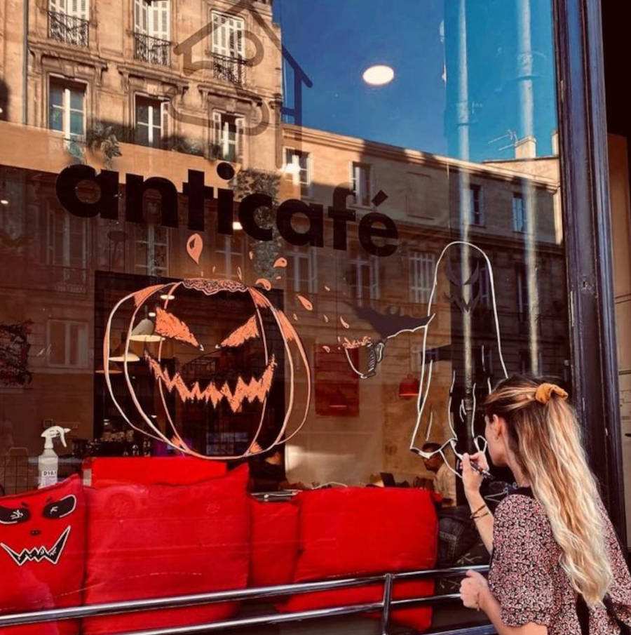 Imagem de menina pintando fantasmas e abóbora para vitrine para o Halloween, com almofadas vermelhas 