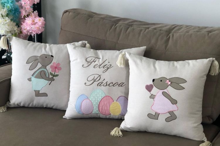 Sofá bege com três almofadas de Páscoa, com coelhos e frase de "Feliz Páscoa"