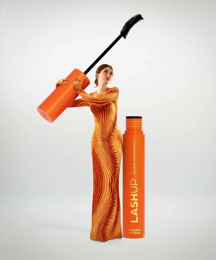 Mari Maria com vestido laranja estampado segura uma escova gigante de rímel ao lado de um frasco em tamanho aumentado. O produto, "Lash Up", é vibrante, em tom laranja, com design clean sobre fundo branco, destacando maquiagem.