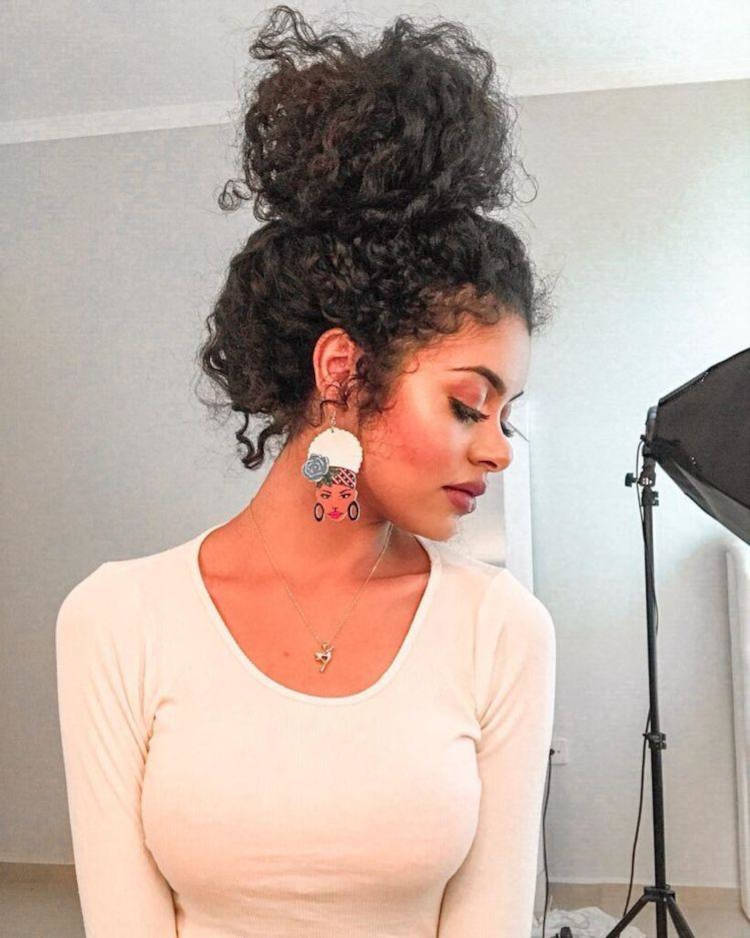 Mulher de pele negra com blusa bege e cabelo cacheado preto em coque volumoso