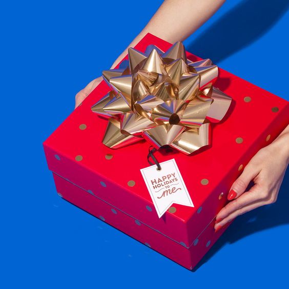 Mãos segurando caixa de presente vermelha com laço dourado em fundo azul