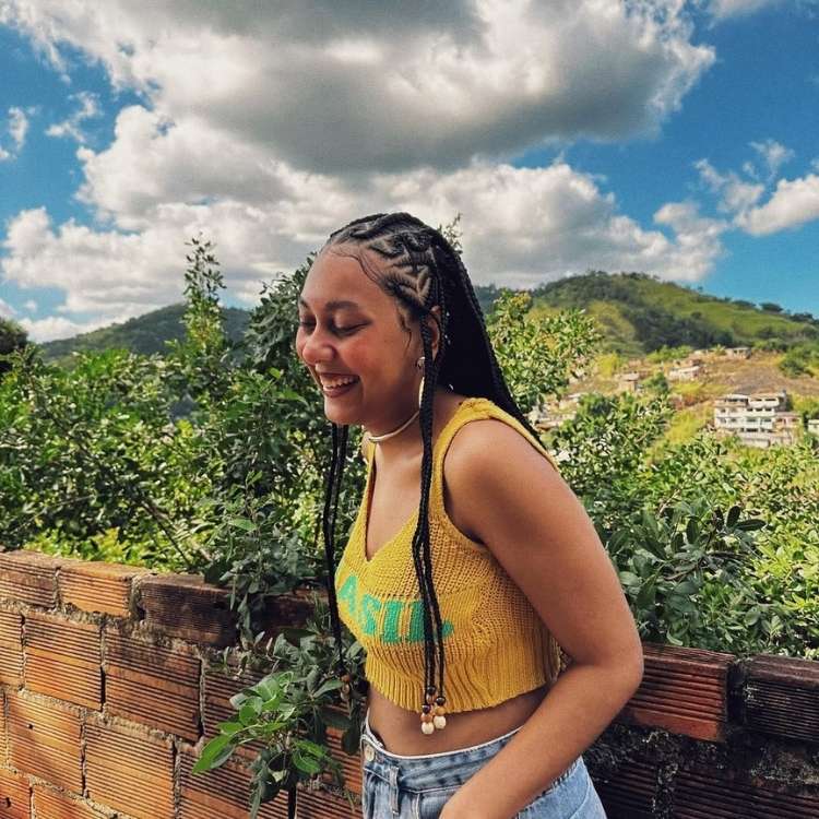 Foto de Thallita Xavier usando tranças no cabelo, uma blusa de crochê amarela e um short jeans