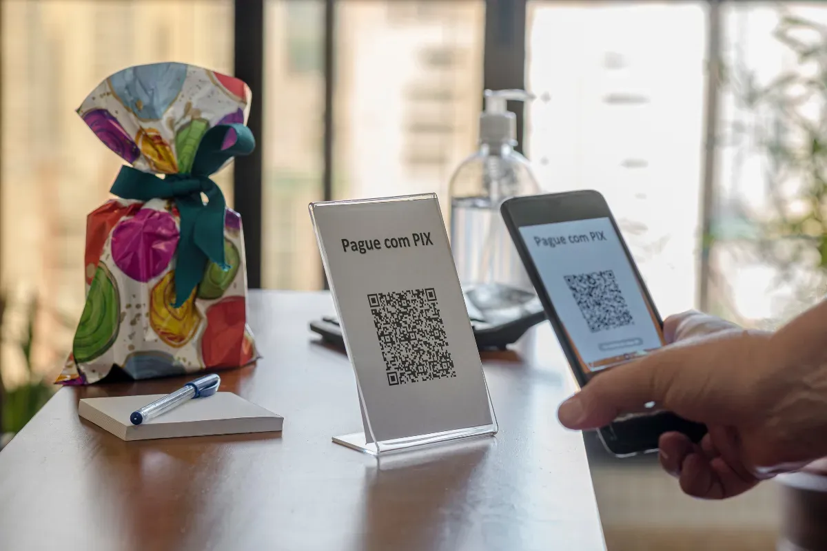 Pessoa usando celular para escanear QR code de pagamento Pix em balcão de estabelecimento