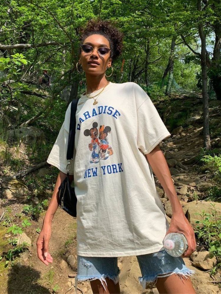 Mulher negra de bermuda jeans, camiseta oversized branca e óculos escuros.