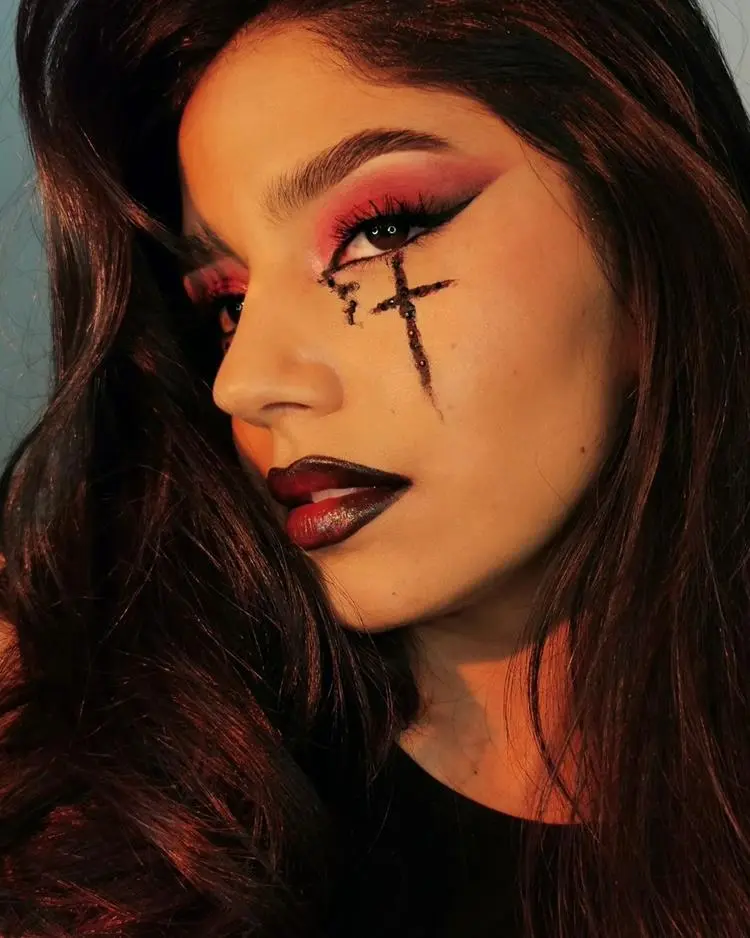 mulher com maquiagem básica em tons avermelhados, desenho de cruz com sangue abaixo dos olhos