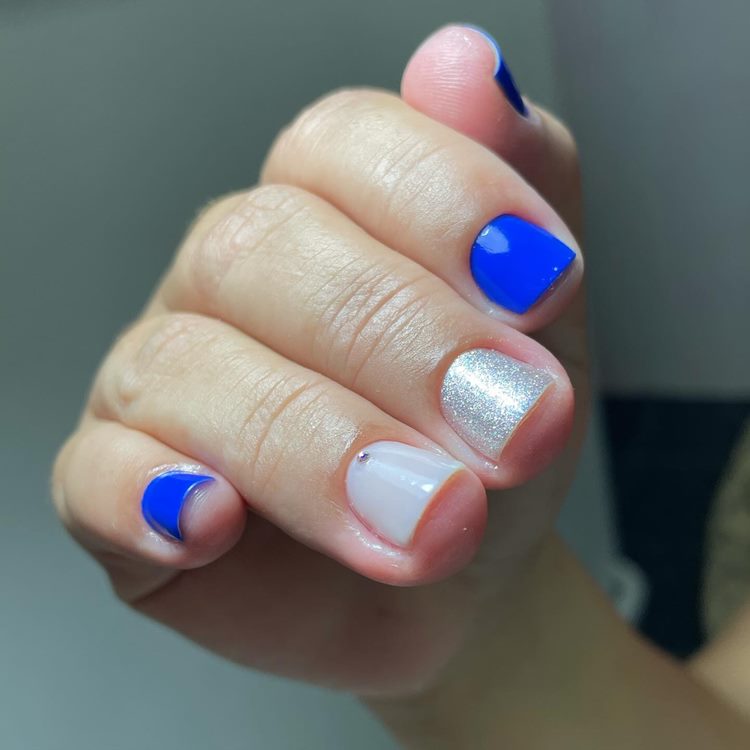 Unhas decoradas em tons de azul com Glitter e uma pedrinha