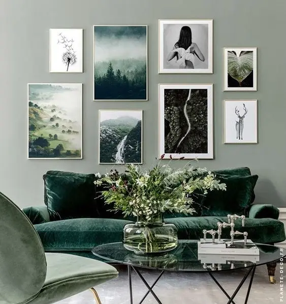 Sala com parede cinza de quadros, sofá verde, poltrona verde e mesa de centro de vidro com decorações
