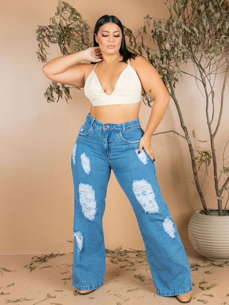 Mulher de pele clara com cropped branco decotado e calça jeans wide leg destroyed
