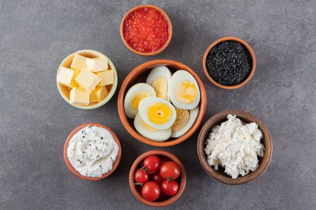 Mesa cinza com tigelas com ovos cozidos, patês, tomates, manteiga e mais