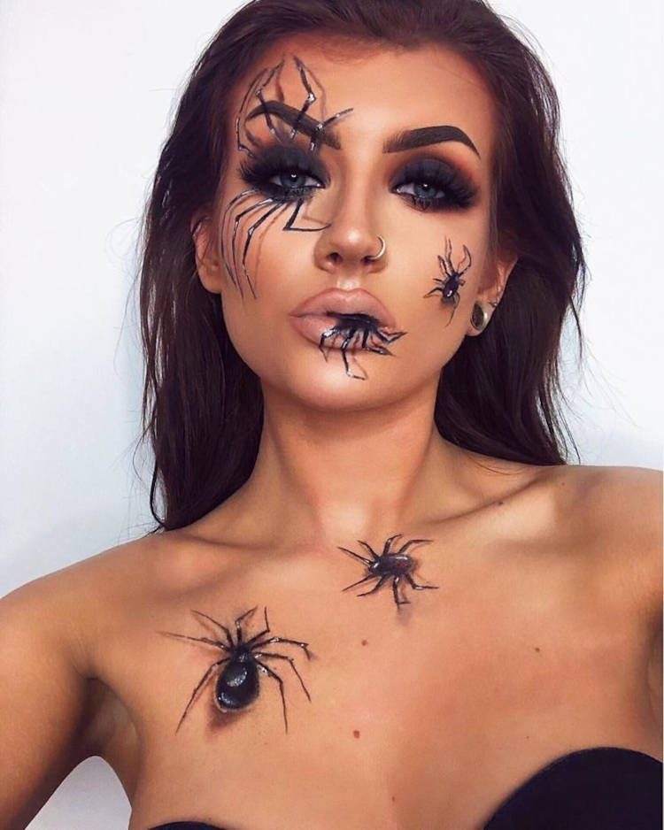 Mulher de pele clara com sombra preta esfumada nos olhos e desenhos de aranhas 3d no rosto, como uma grande no olho, média na bochecha, saindo da boca e andando pela clavícula 