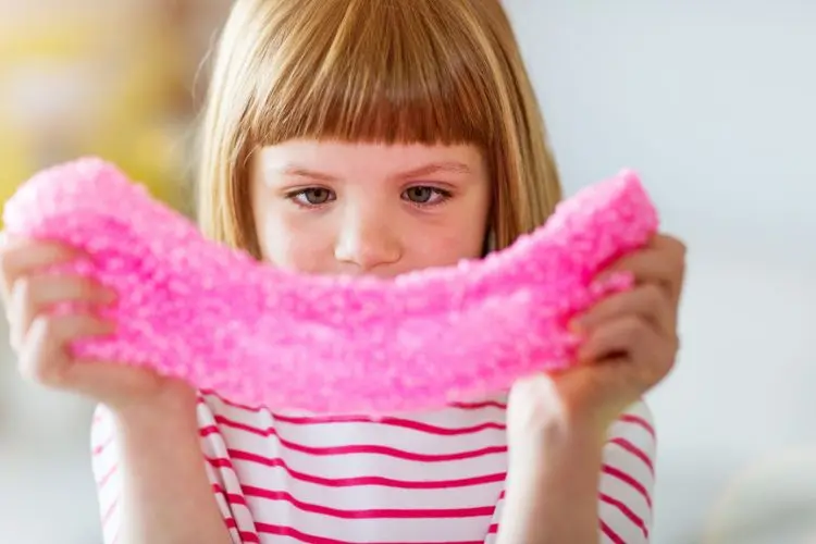 A imagem mostra uma criança concentrada segurando uma massa sensorial rosa, esticando-a com as mãos. Esse tipo de massa é um dos presente para criança com autismo, pois ajuda a desenvolver habilidades motoras e sensoriais. A criança está vestida com uma camiseta listrada, e o ambiente parece ser iluminado e acolhedor, propício para brincadeiras.


