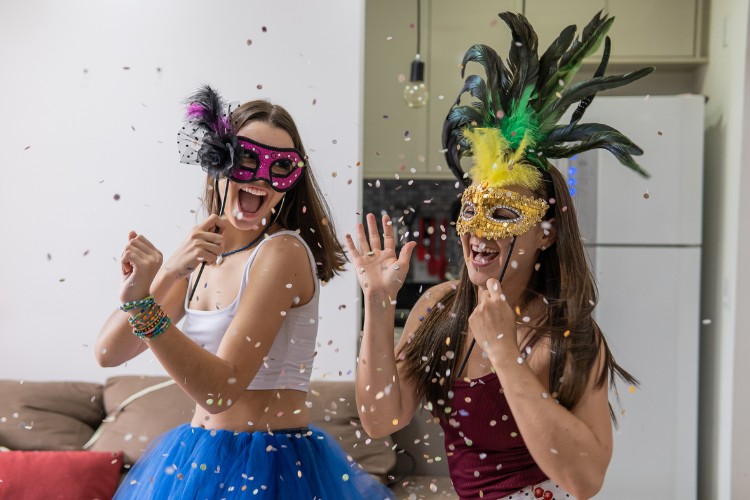 Duas mulheres de pele clara com máscara de Carnaval curtindo em casa 