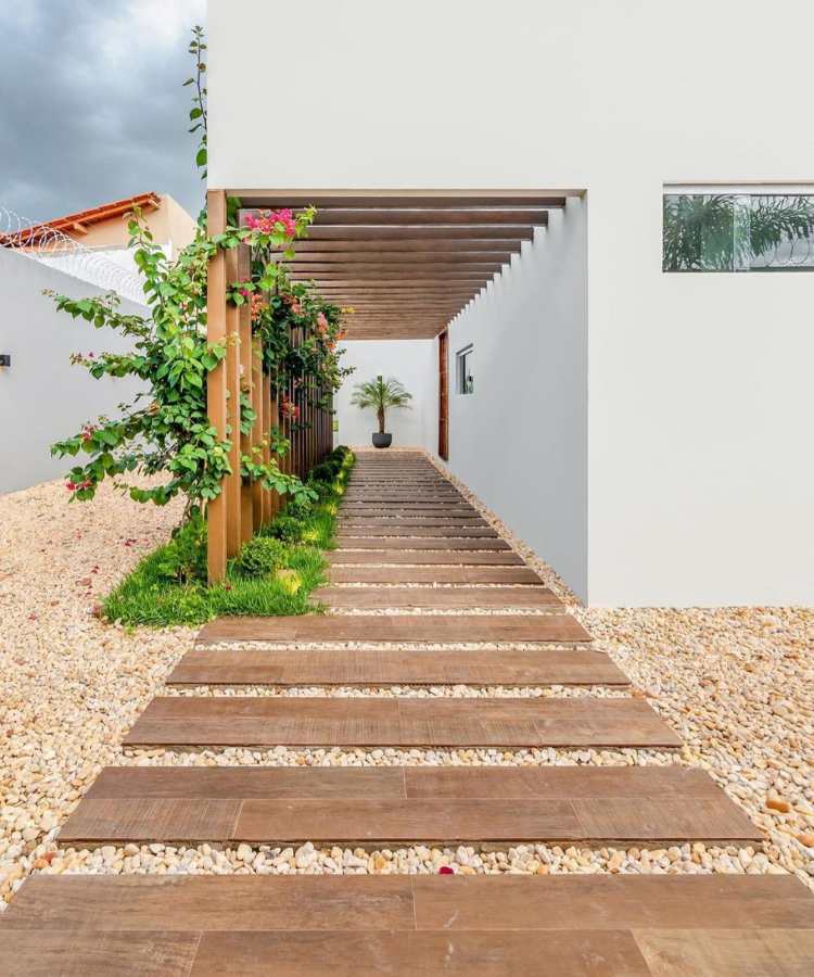 Caminho de jardim com pedra seixo de rio e plantas ao redor de pergolado de casa