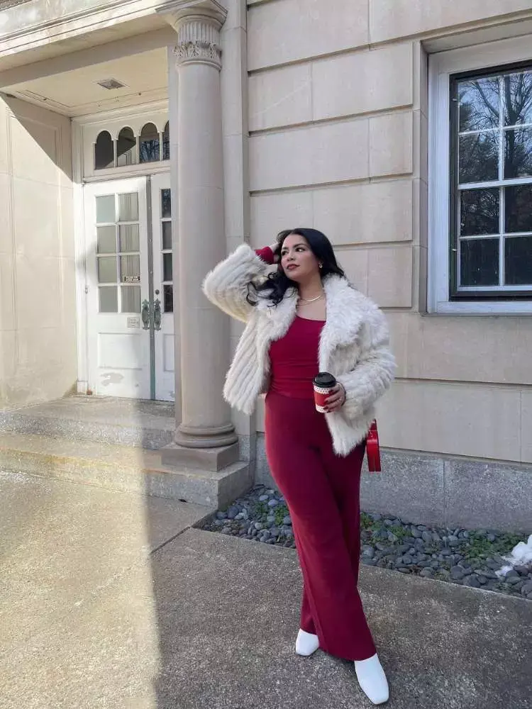 Mulher de pele clara usando blusa vermelha, calça vermelha e casaco branco de pele 