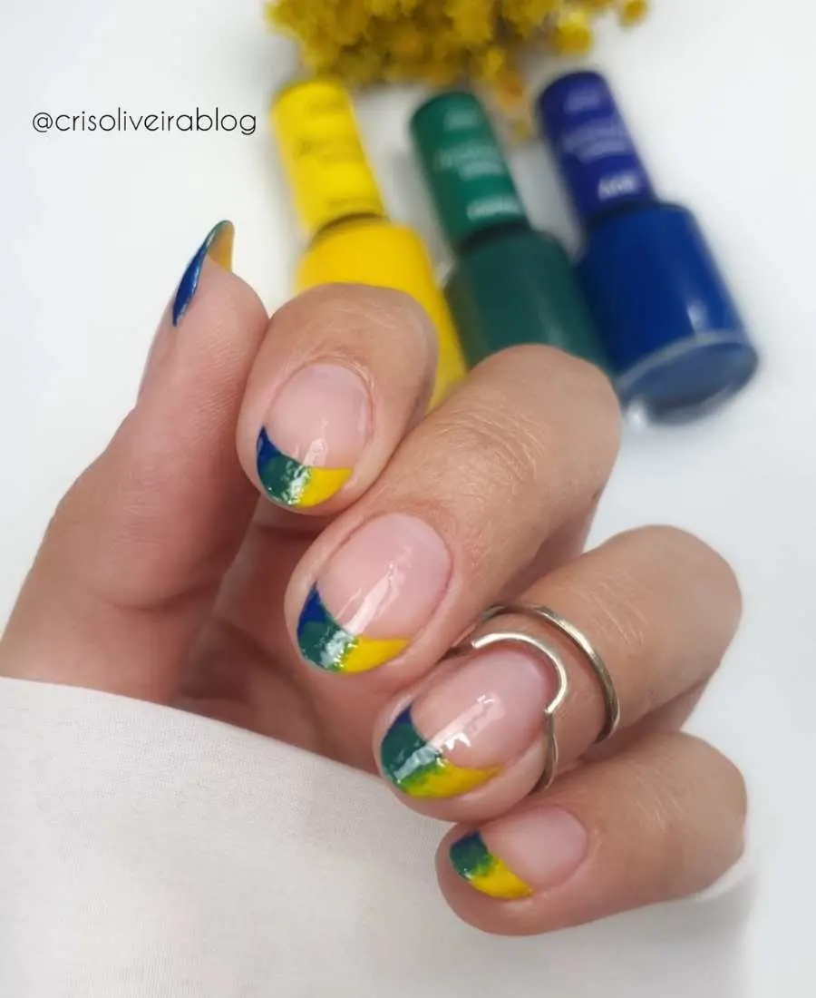 Imagem de mão com unhas decoradas de Brasil.  Cores usadas, verde, amarelo e azul. Francesinha com as cores mescladas em todas as unhas.