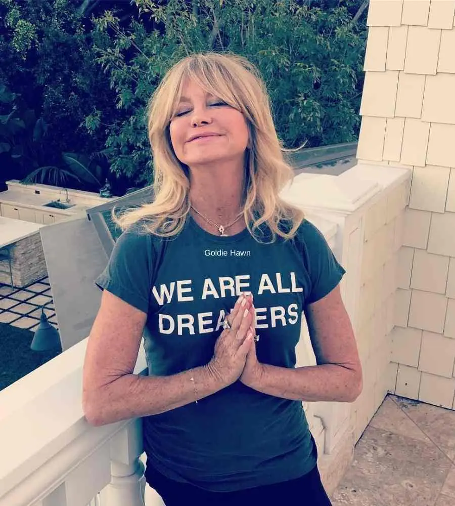 Goldie Hawn com as mãos orando, de olhos fechados e em sacada com pedras - famosas mais 70 anos.