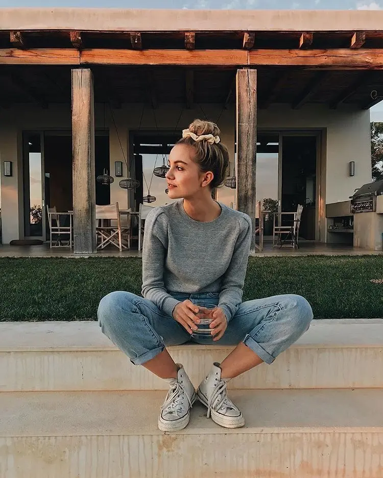 Frase para foto pensativa mulher sentada na escada segura copo de água, usa coque e veste tênis branco, calça jeans e moletom cinza
