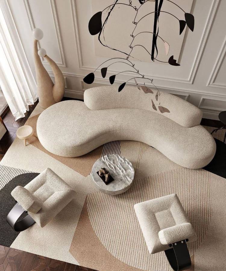 A imagem apresenta uma sala moderna com sofá curvo bege, poltronas geométricas e uma mesa central de mármore. O tapete com padrões suaves complementa o ambiente. Dicas de decoração para quem tem TDAH incluem espaços minimalistas e móveis funcionais.