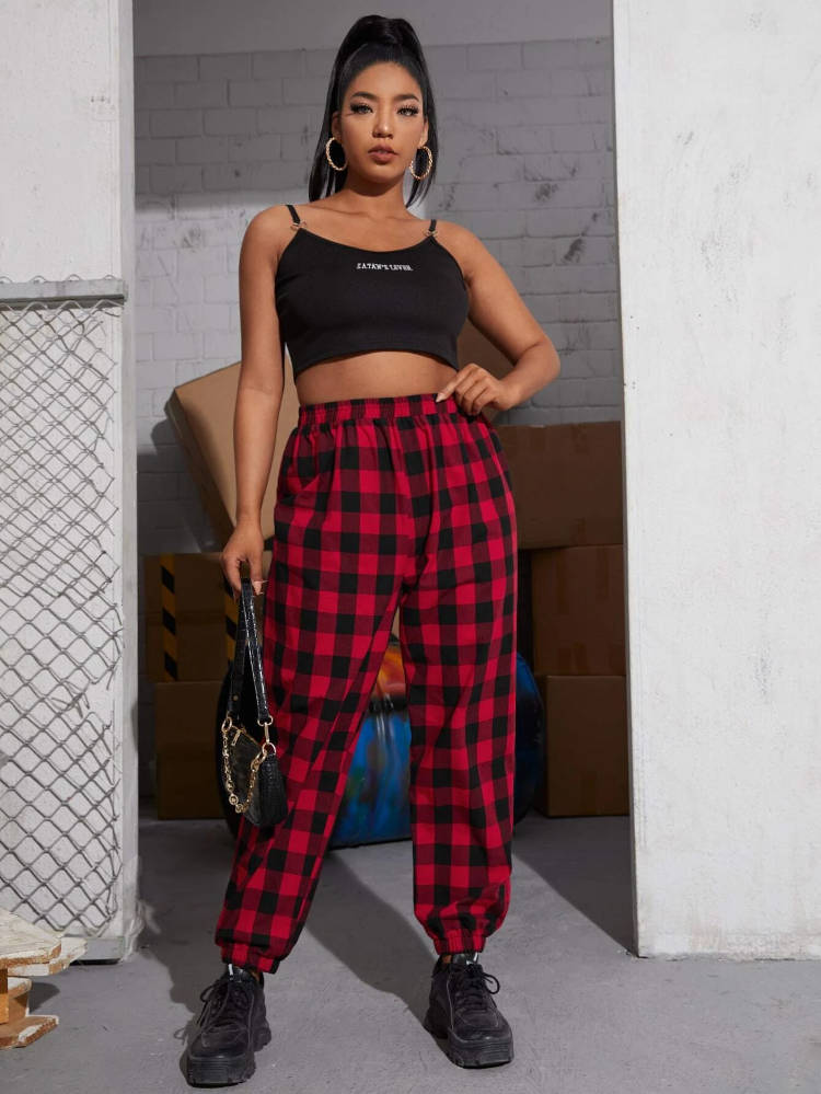 Mulher morena usando top preto e calça xadrez vermelha e preto.