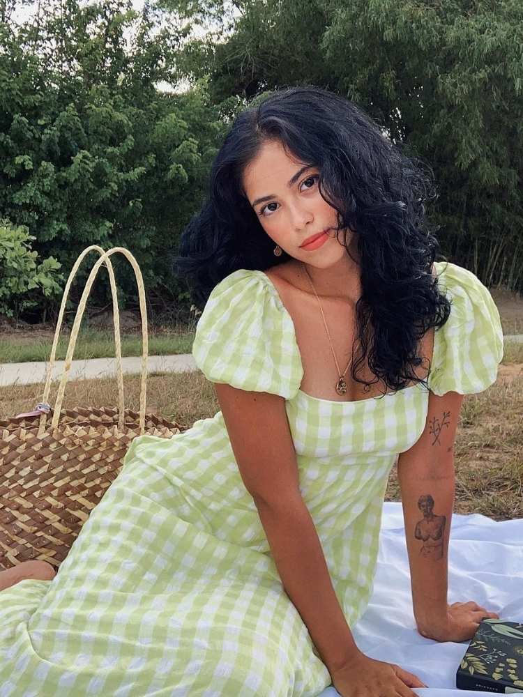 Mulher de pele morena com vestido xadrez branco e verde xadrez de manga bufante