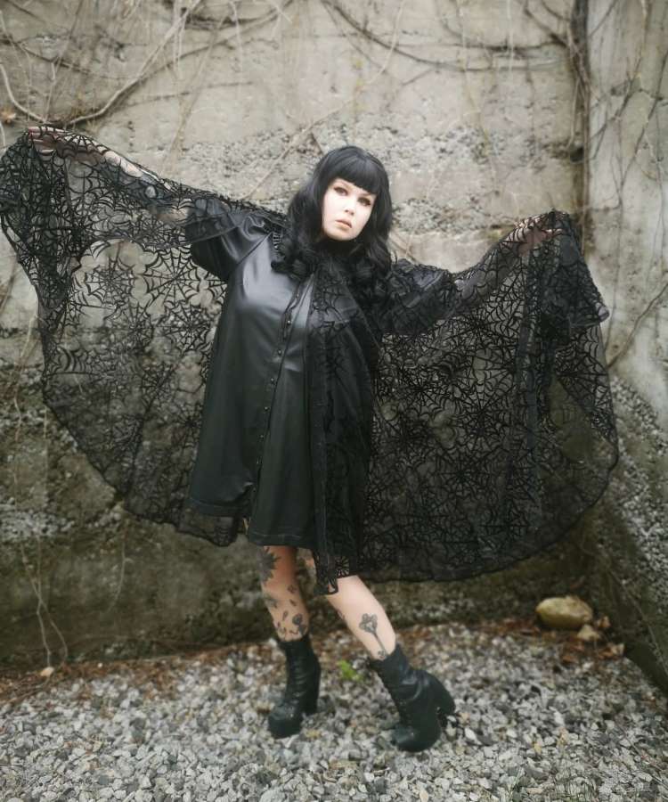 Mulher de pele clara usando vestido preto e capa de teia de aranha de tule 