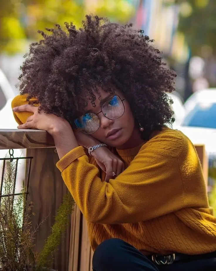 Frase para foto pensativa mulher negra com black power, óculos de gatinho, moletom de tricô mostarda, cinto e calça preta Frase para foto pensativa mulher negra
