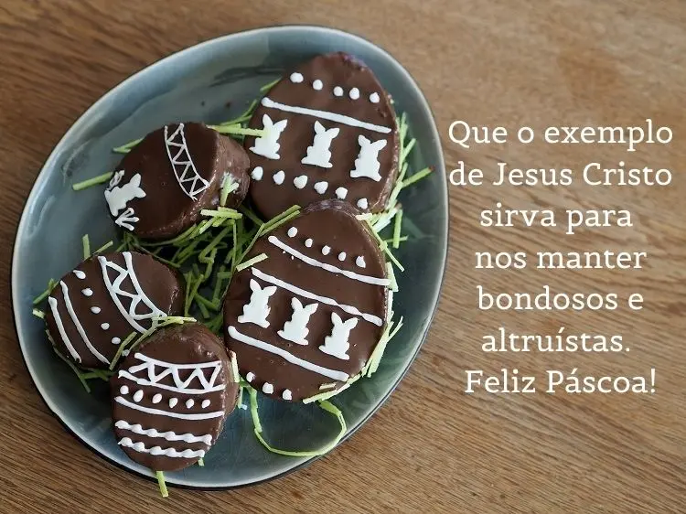 Mesa de madeira com prato com doces de páscoa e frase: Que o exemplo de Jesus Cristo sirva para nos manter bondosos e altruístas. Feliz Páscoa!