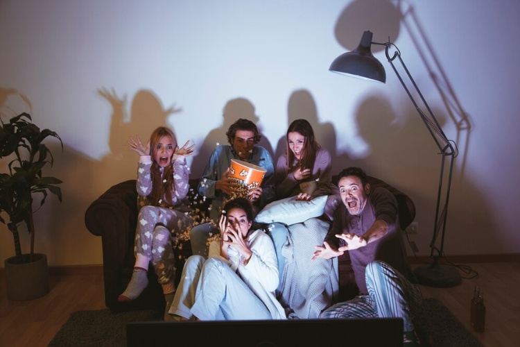 Pessoas de pele clara vendo filme de terror entre amigos, com luzes apagadas e pipoca