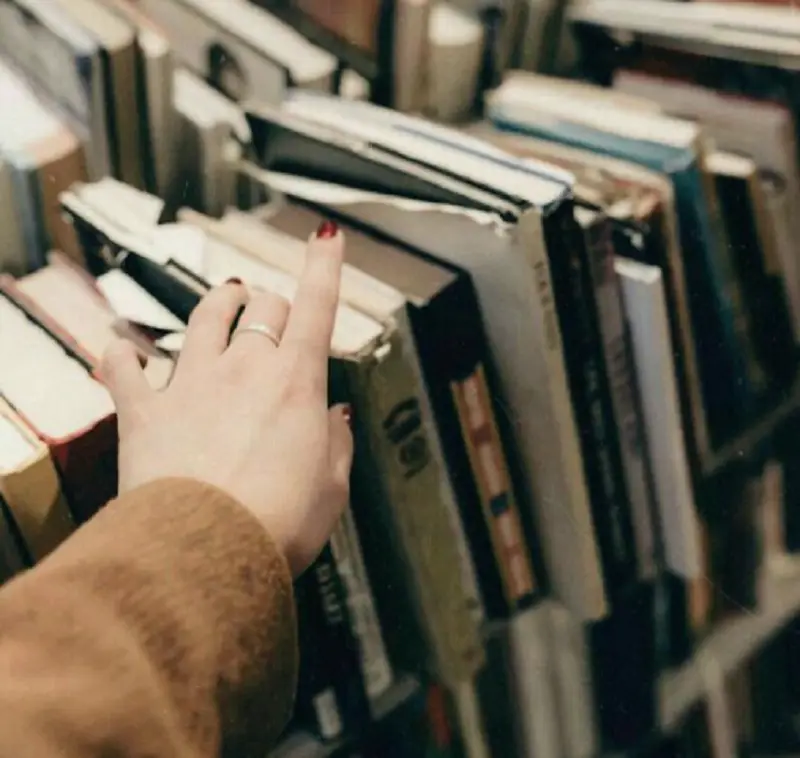 mão feminina procurando livros em estante mão feminina sobre livros em uma estante