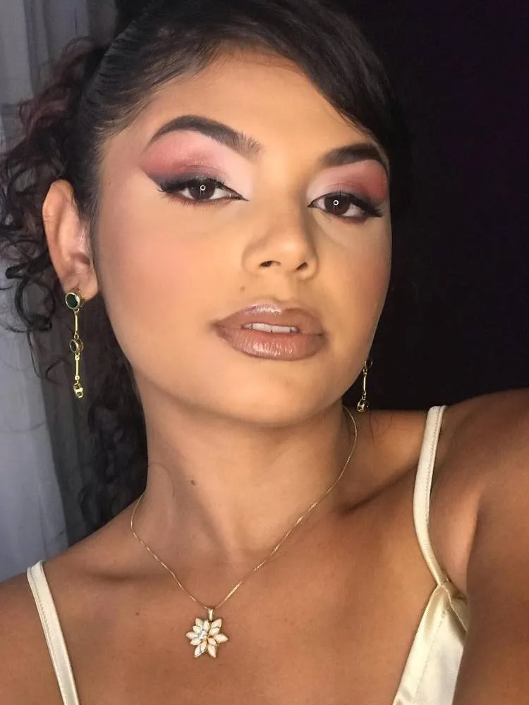 Mulher de pele morena com sombra esfumada rosa e preta, além de batom e gloss marrom 